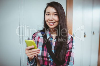 Cheerful student standing next the locker and using smartphone