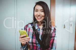 Cheerful student standing next the locker and using smartphone
