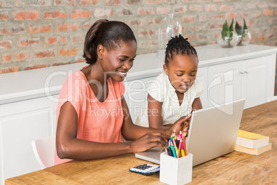 Cute daughter using laptop at desk with mother