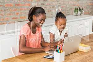 Cute daughter using laptop at desk with mother