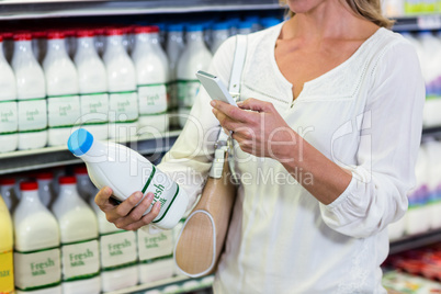Woman using smartphone while holding milk bottle