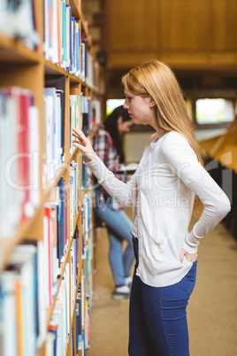 Blond student looking for book in library shelves