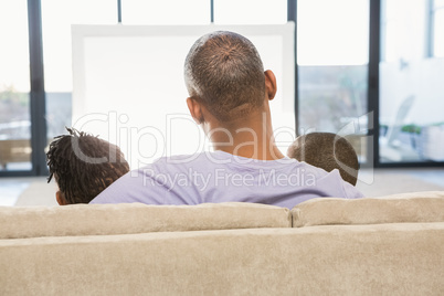 Two children sitting on sofa with their father