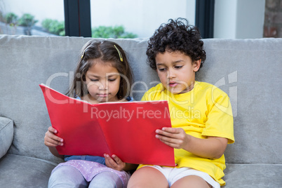 Cute siblings reading a book on the sofa