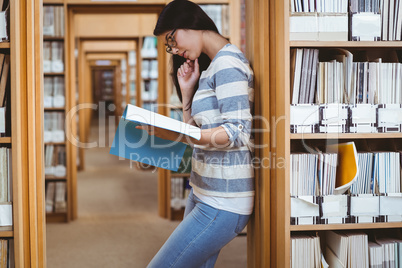 Focused student leaning against bookshelves and reading a book i Focused student leaning against bookshelves and reading a book i