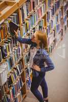 Blond student picking book from bookshelf