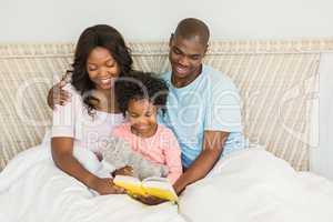 Pretty couple with her daughter reading a book in bed
