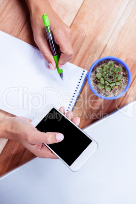 Feminine hands holding smartphone and taking notes