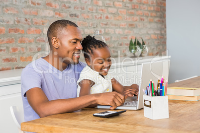 Cute daughter using laptop at desk with father