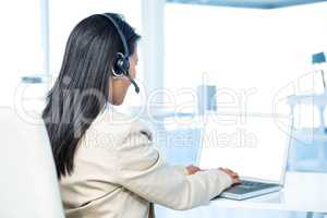Rear view of businesswoman with headset using laptop