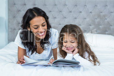 Happy mother and daughter reading a book on the bed