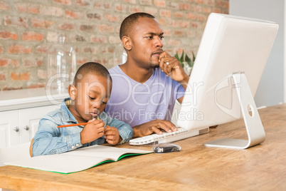 Cute son doing his homework with father