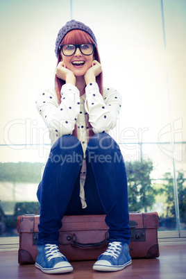 Smiling hipster woman sitting on suitcase