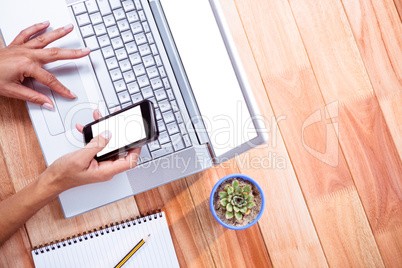 Overhead of feminine hands using laptop and smartphone