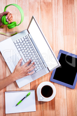 Overhead of feminine hands typing on laptop and holding headphon