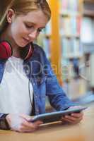 Pretty student with headphones using tablet in library
