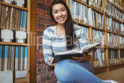 Smiling student sitting on the floor against wall in library rea