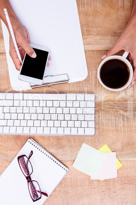 Businesswoman holding smartphone and coffee cup