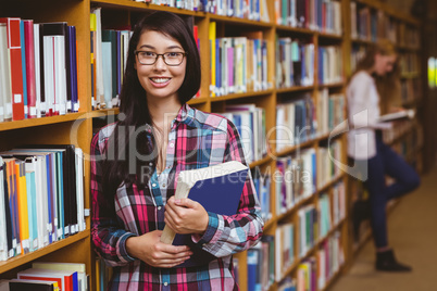 Smiling student leaning against bookshelves holding book