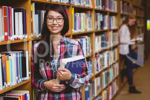 Smiling student leaning against bookshelves holding book