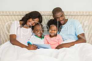 Family with digital tablet in bed