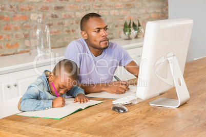 Cute son doing his homework with father