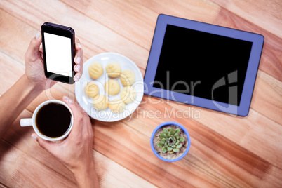 Overhead of feminine hands holding smartphone and coffee