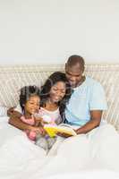 Pretty couple with her daughter reading a book in bed