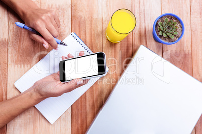 Overhead of feminine hands holding smartphone and taking notes