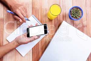 Overhead of feminine hands holding smartphone and taking notes