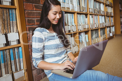 Smiling student sitting on the floor against wall in library usi