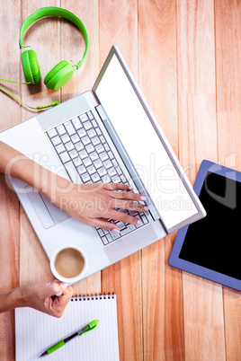 Overhead of feminine hands using laptop and holding coffee