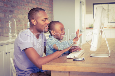 Cute son using laptop at desk with father