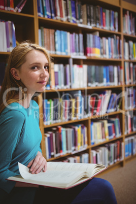 Pretty student sitting on chair holding book in library