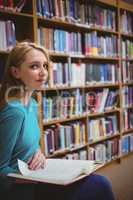 Pretty student sitting on chair holding book in library