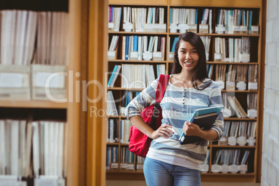 Pretty student standing in library holding a book
