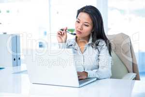 Smiling businesswoman with pen using laptop