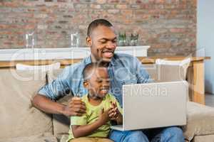 Father and son using laptop on the couch