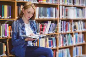 Pretty student sitting on chair reading book in library