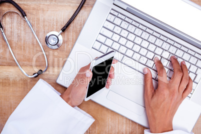 Doctor using smartphone and laptop on wooden desk