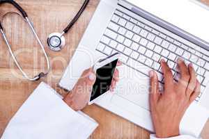 Doctor using smartphone and laptop on wooden desk