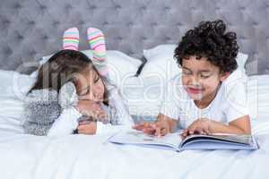 Cute siblings reading a book on the bed