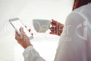 Woman with red hair using smartphone and holding coffee cup