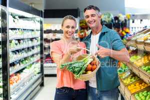 Smiling couple pointing basket with vegetables
