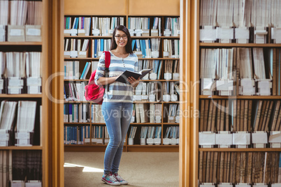 Pretty student with backpack reading a book in library