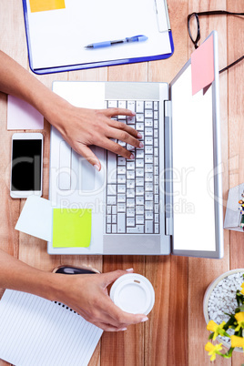 Overhead of feminine hands using laptop and holding coffee mug