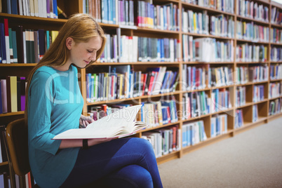 Smiling student sitting on chair reading book in library