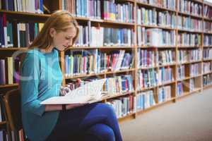 Smiling student sitting on chair reading book in library