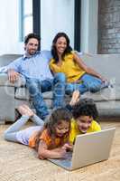 Children laying on carpet in living room using laptop