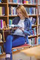 Pretty student sitting on chair reading book in library